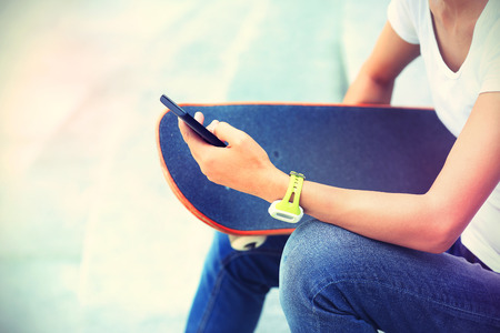 closeup of young woman skateboarder use smart phone in cityの写真素材