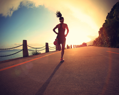 young fitness woman running on sunrise seaside trailの写真素材