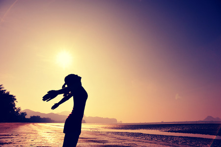 cheering young woman open arms on sunrise beachの写真素材