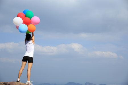 cheering young asian woman on mountain peak rock with colored balloonsの写真素材