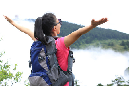 woman hiker open arms at peak of  mountain