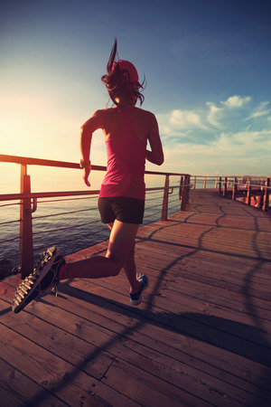 healthy lifestyle sports woman running on wooden boardwalk sunrise seasideの写真素材