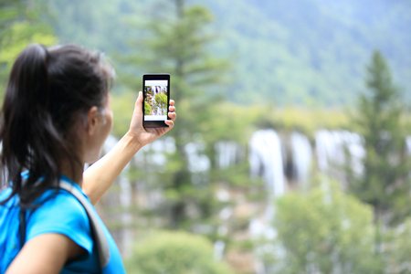 woman tourist taking photo with cellphone in jiuzhaigou national park,chinaの写真素材