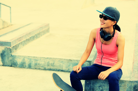 woman skateboarder listening music from cellphone mp3 player on skateparkの写真素材