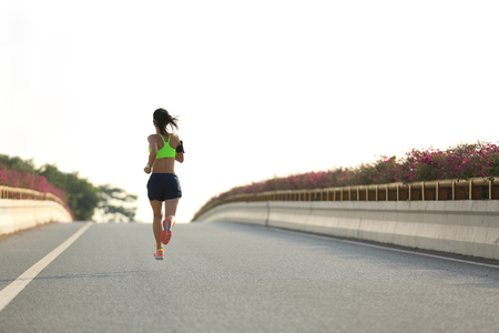 young woman runner running on city bridge roadの写真素材