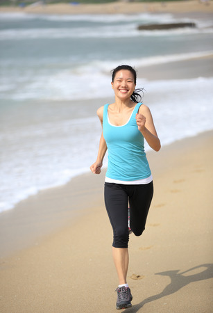 sporty lifestyle asian woman running at beach with spraying sea waterの写真素材