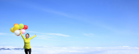 young cheering woman running with colorful balloons on mountain peakの写真素材