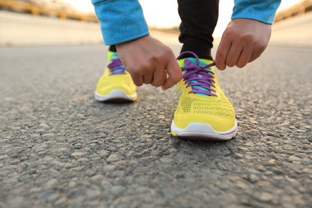 young woman runner tying shoelaces on city roadの写真素材