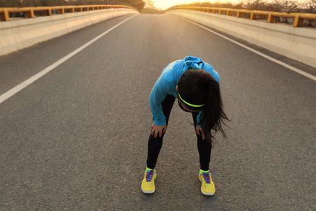 tired woman runner taking a rest after running hard on city roadの写真素材