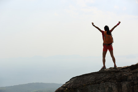 cheering woman hiker open arms at mountain peakの写真素材