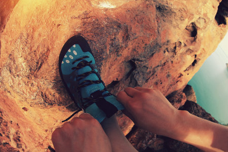 young woman rock climber tying shoelace at mountain rock