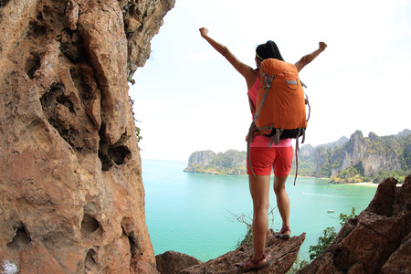 cheering young asian woman hiker open arms on seaside mountain peakの写真素材