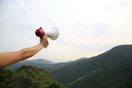 hand hold loudspeaker to blue sky on mountain peakの写真素材