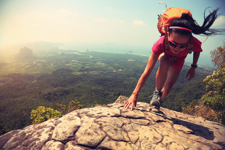 young asian woman hiker climbing rock on mountain peak cliffの写真素材