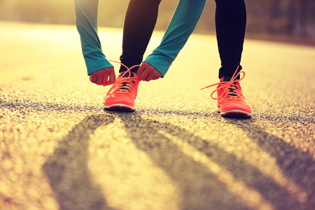 young fitness woman runner tying shoelace on roadの写真素材