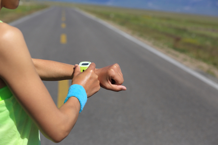 young woman runner ready to run set and looking at sports smart watch, checking performance or heart rate pulse trace. sport and fitness outdoors .の写真素材