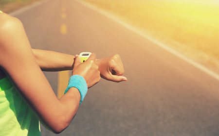 young woman runner ready to run set and looking at sports smart watch, checking performance or heart rate pulse trace. sport and fitness outdoors .の写真素材