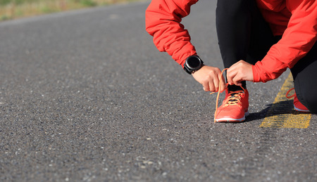 young woman runner tying shoelace on country roadの写真素材
