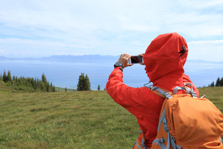 woman hiker taking photo with smart phone at mountain peakの写真素材