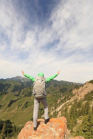 cheering successful woman backpacker open arms on mountain peakの写真素材
