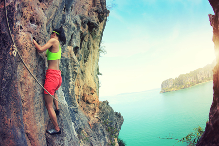 young woman rock climber climbing at seaside mountain rockの写真素材