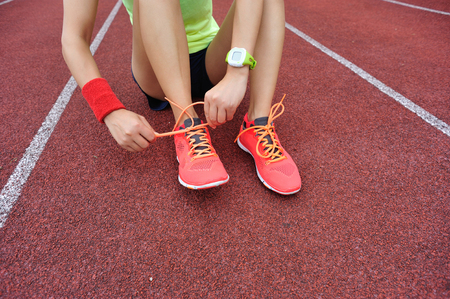 young woman runner tying shoelaces on tracksの写真素材