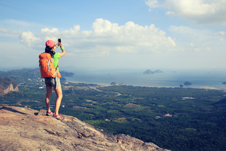 hiker taking photo with smartphone at seaside mountain cliffの写真素材