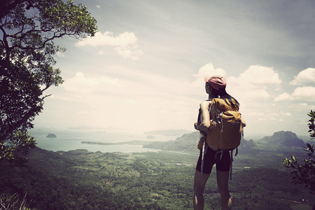 young traveler with backpack standing on the mountain peak observing localityの写真素材