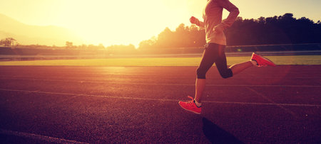 Young woman running during sunny morning on stadium track
