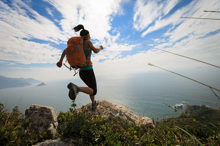 successful hiker jumping on seaside mountain peak rockの写真素材