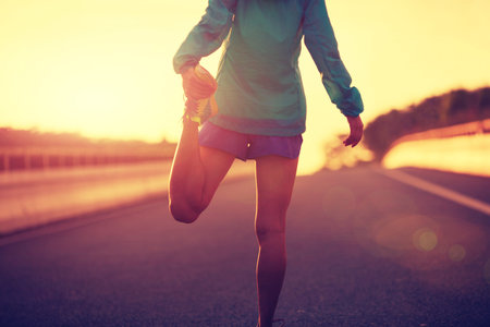 young fitness woman runner stretching legs on city road