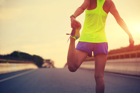 young fitness woman runner stretching legs on city roadの写真素材