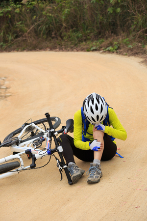female cyclist getting injured while falling from mountain bike on forest trailの写真素材