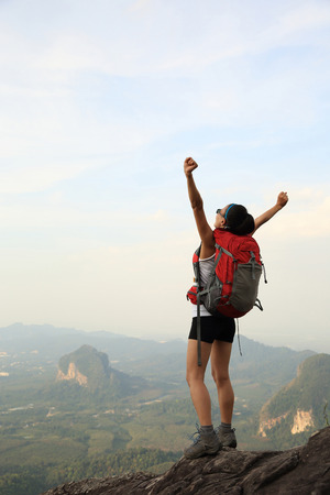cheering young woman backpacker at  mountain peakの写真素材