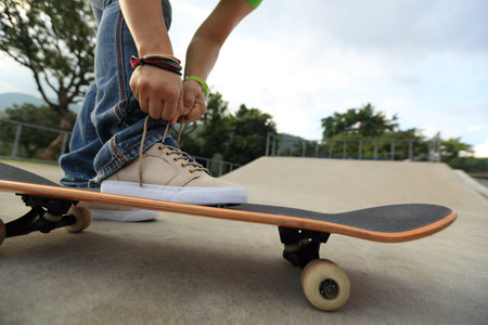 young skateboarder tying shoelace on skateboard at skatepark rampの写真素材