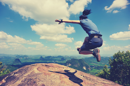 cheering successful young woman jumping on mountain peakの写真素材