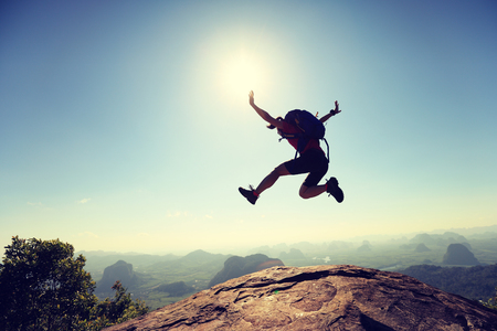 cheering successful young woman hiker jumping on mountain peakの写真素材