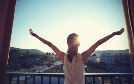 young woman open arms face the sunrise on balconyの写真素材