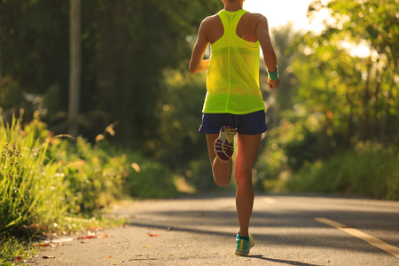 Young fitness woman running on morning tropical forest trailの写真素材