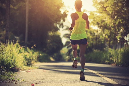 Young fitness woman running on morning tropical forest trailの写真素材