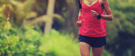 Young fitness woman running at morning tropical forest trailの写真素材