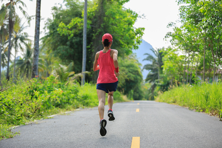 Young fitness woman running at morning tropical forest trailの写真素材