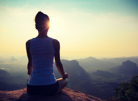 young fitness woman meditating on sunrise mountain peakの写真素材
