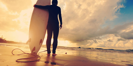 Rear view of young woman surfer with white surfboard on a beach at sunrise