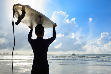 young woman surfer with white surfboard walking to the seaの写真素材