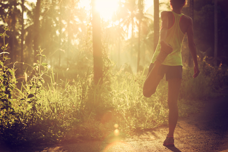 Young female runner stretching legs before running at morning forest trailの写真素材