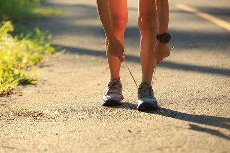 Young fitness woman runner tying shoelace on morning tropical forest trailの写真素材