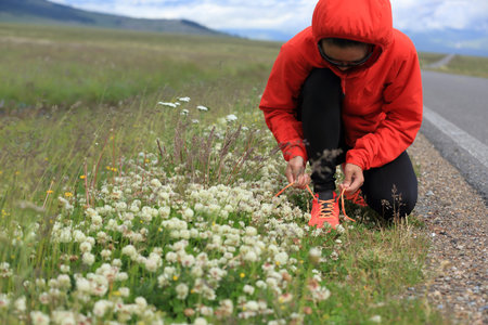 Young woman runner tying shoelace on countryroad
