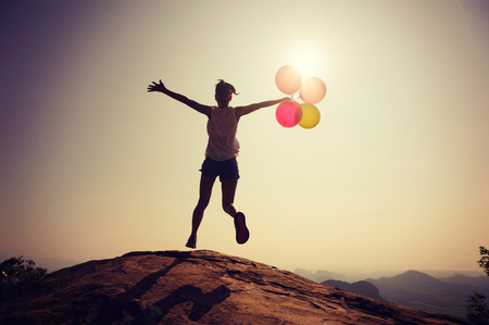 Silhouette of young woman jumping on mountain top with balloonsの写真素材