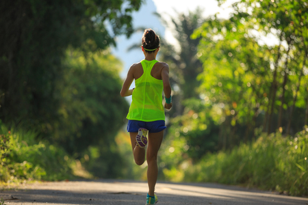 Young fitness woman running at tropical forest trailの写真素材